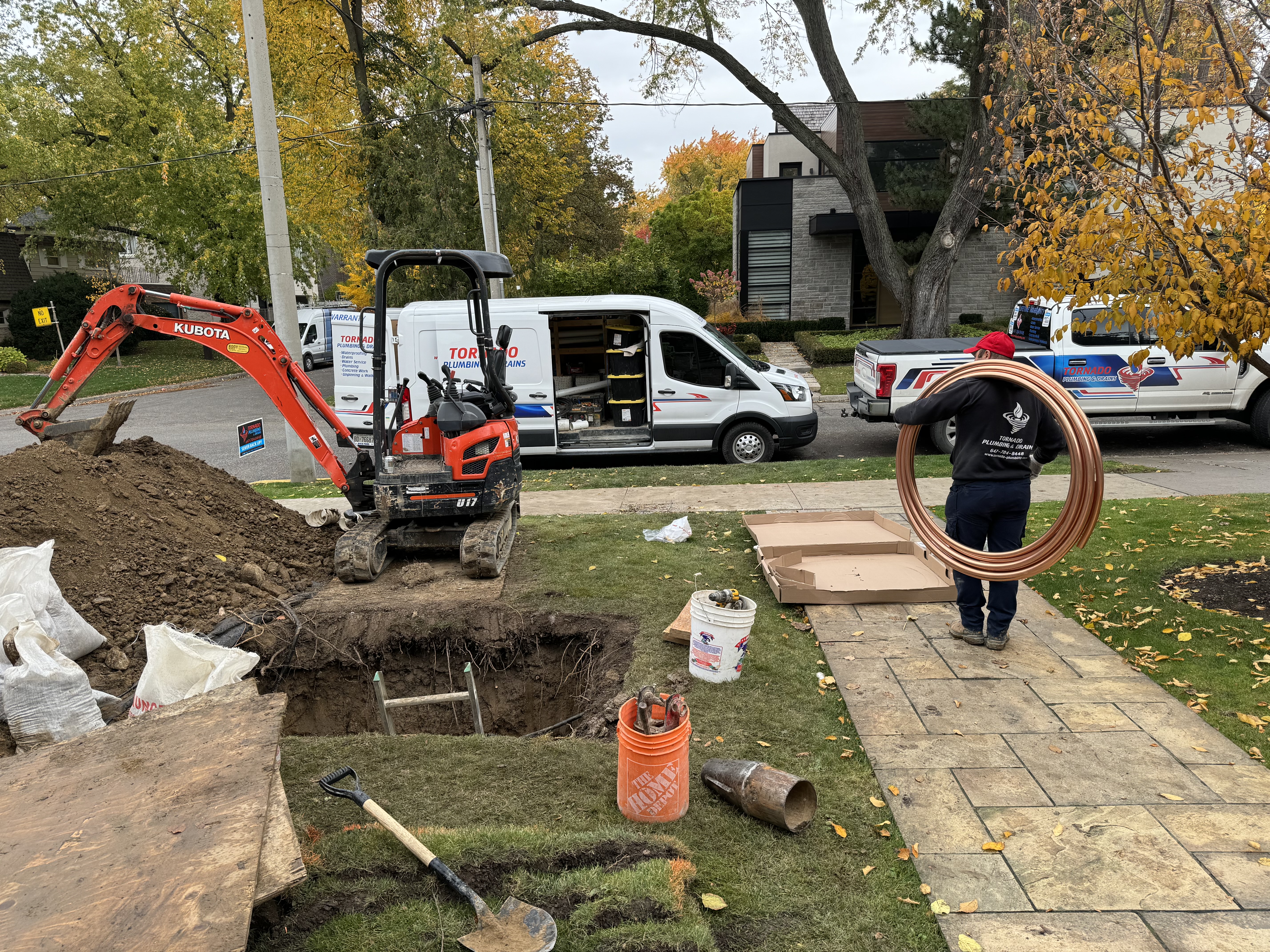 Excavation site in a front yard with service vehicles and copper water-service materials