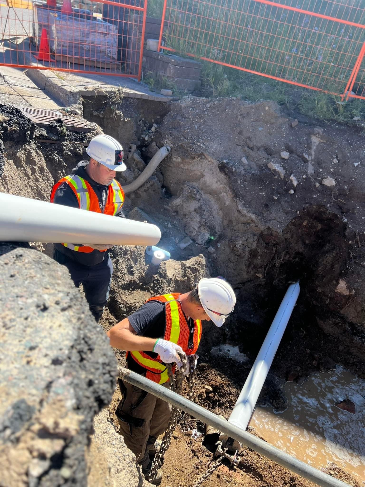 Two crew members working in a deep excavation during sewer-line replacement
