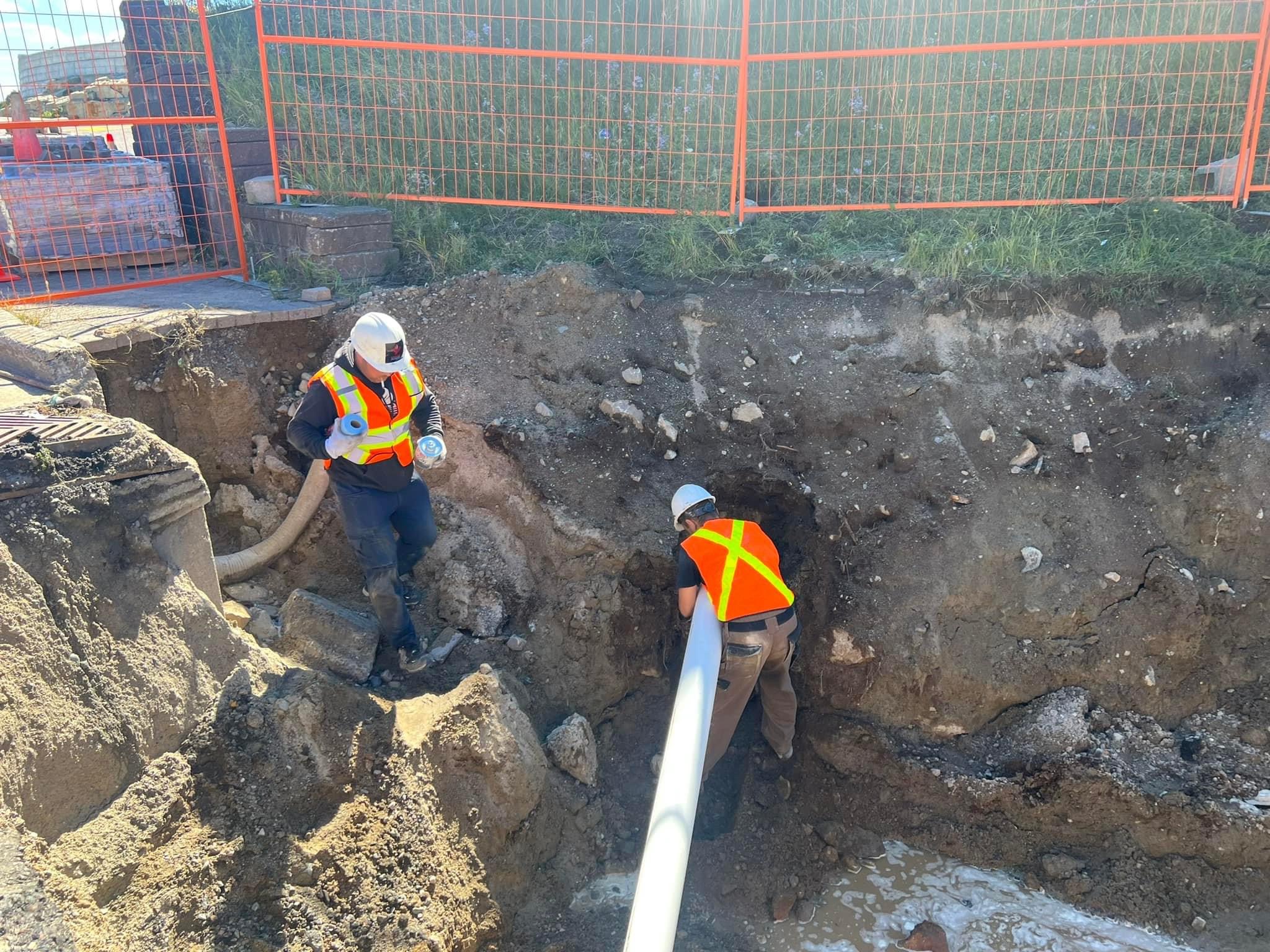 Crew installing a large-diameter pipe in an open excavation during sewer-line work