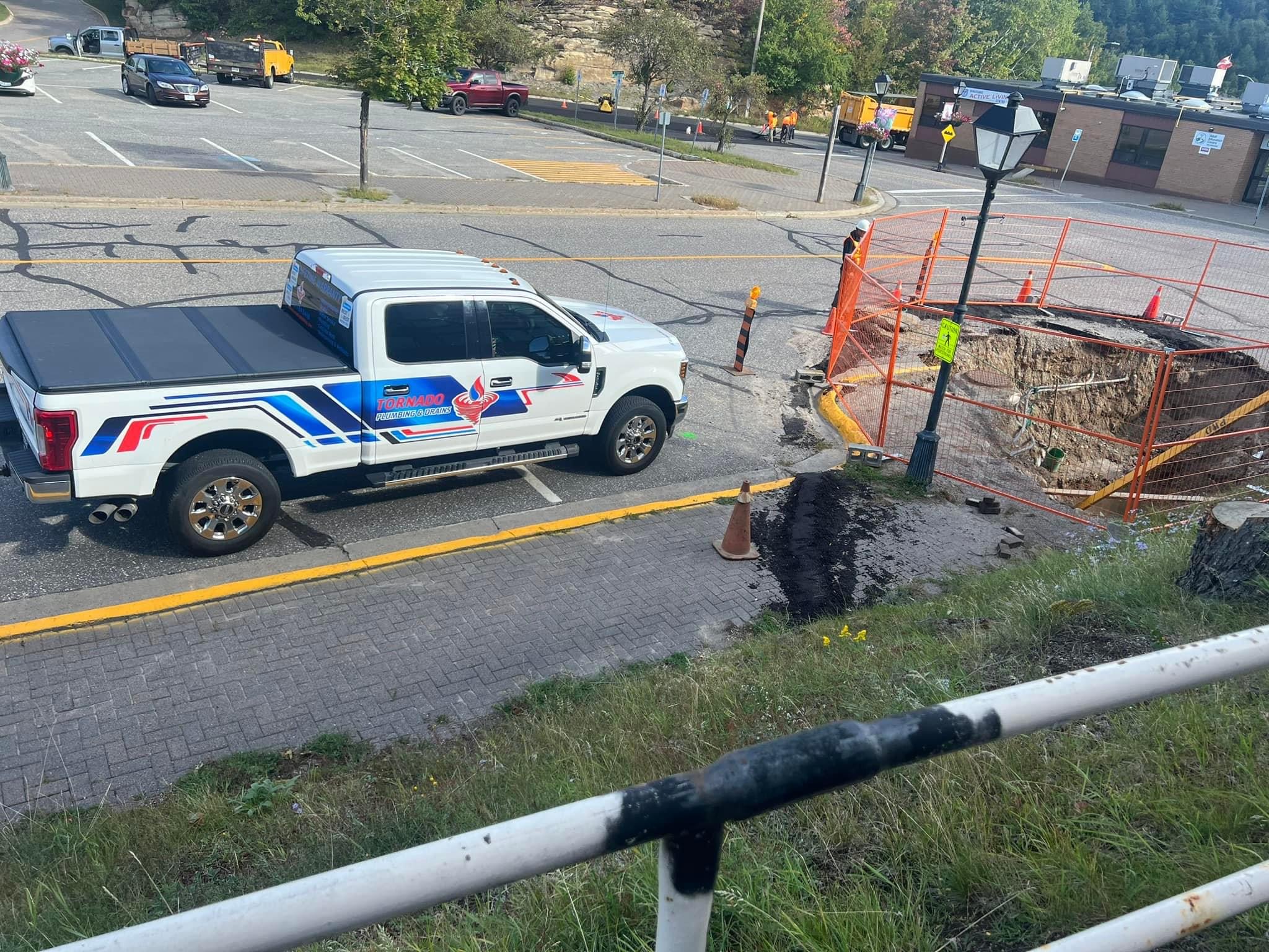 Service truck parked beside a fenced excavation during open-cut sewer-line work