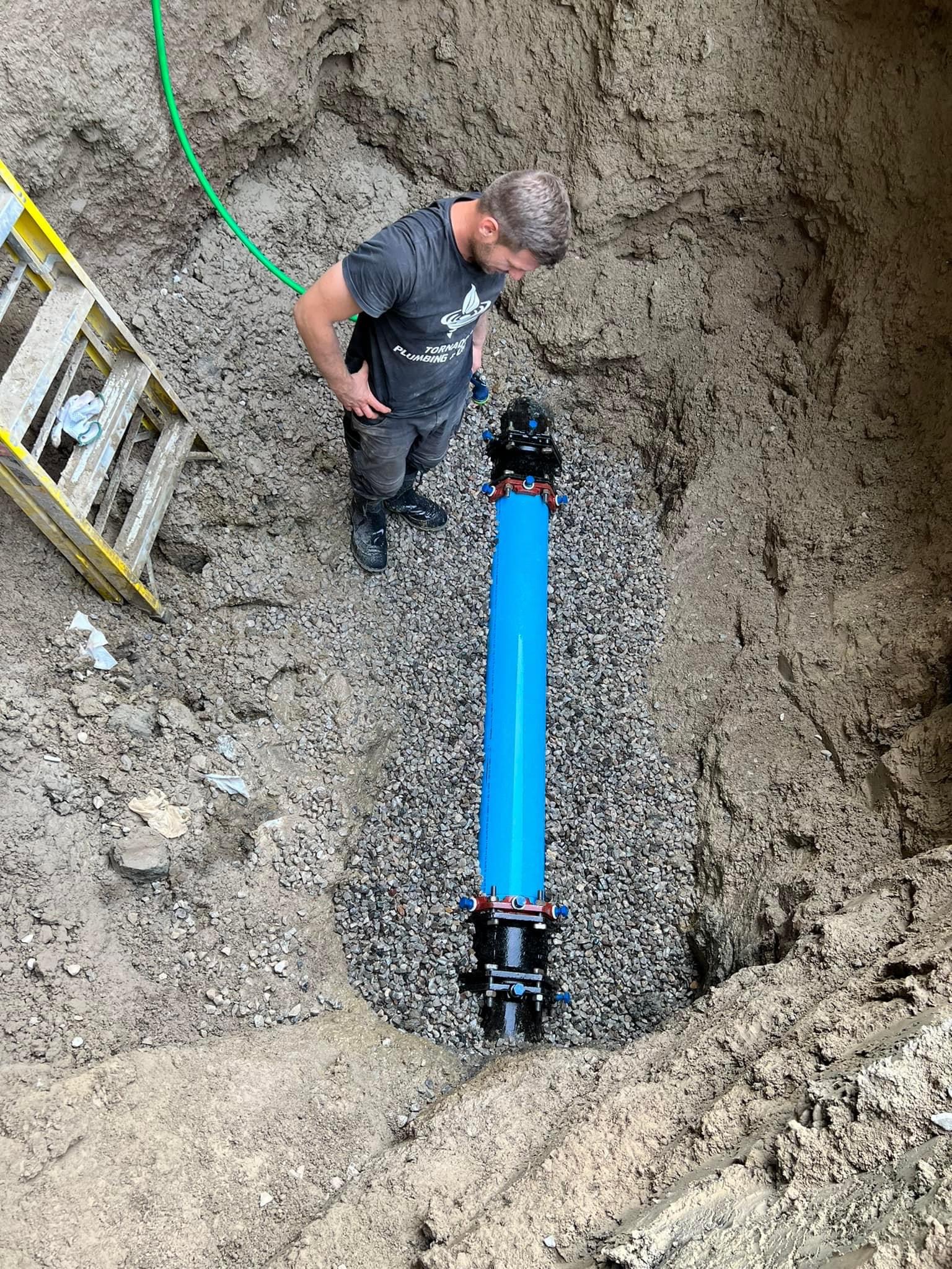 Technician in an excavation trench beside a new blue service line during underground replacement work
