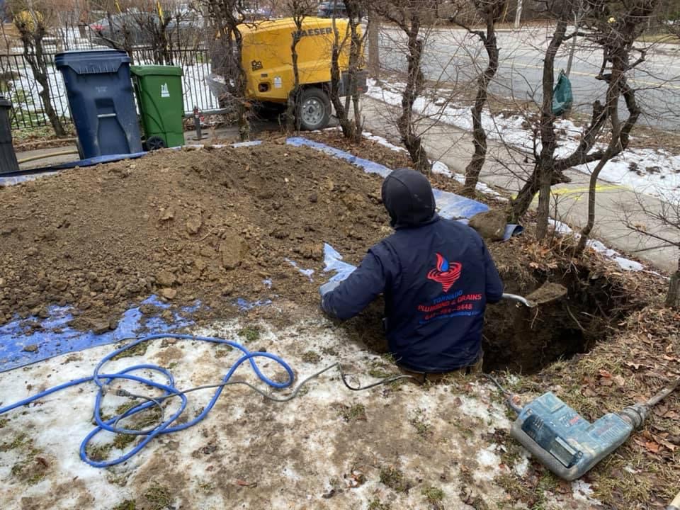 Technician working beside a winter excavation for buried line repair near a driveway