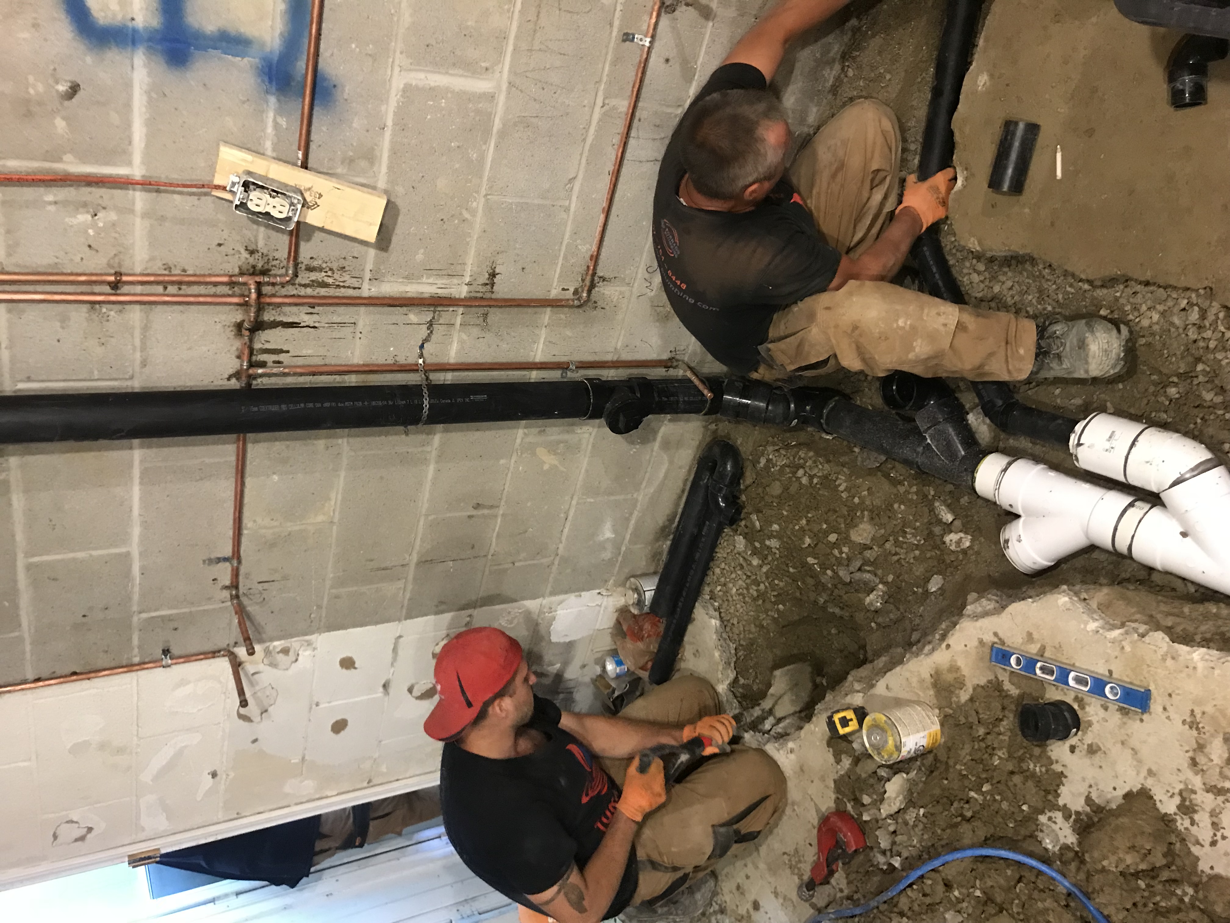 Two technicians installing black ABS drain lines during a basement plumbing rough-in