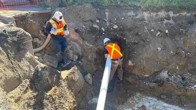 Crew installing a large-diameter pipe in an open excavation during sewer-line work