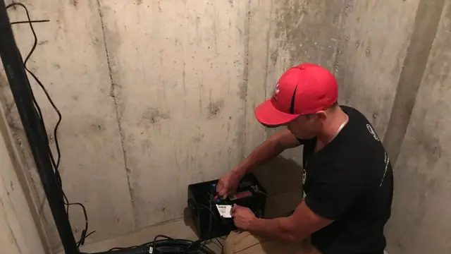 Technician wiring and testing a battery backup sump pump system in a basement