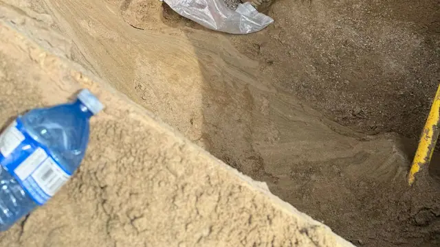 Tornado Plumbing technician kneeling in a deep sewer excavation, setting new sewer pipe on a gravel bed with a green PVC riser beside him