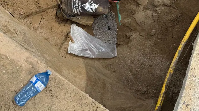 Technician in a Tornado Plumbing and Drains shirt connecting a green PVC cleanout riser to the new sewer line at the bottom of a deep trench