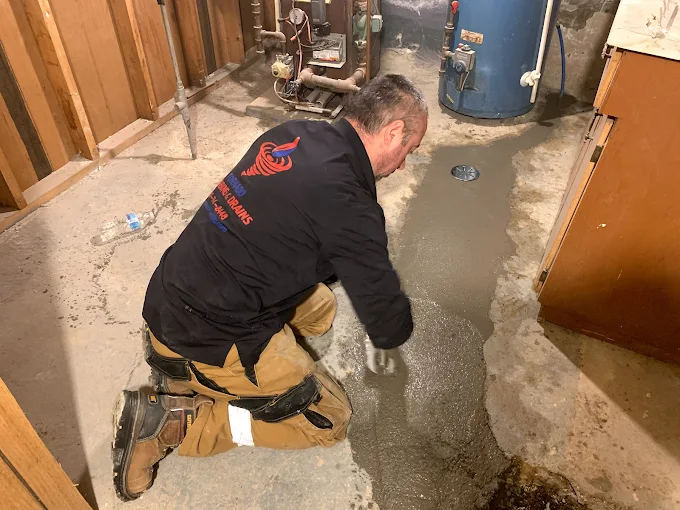 Technician smoothing fresh concrete patch after basement flood-prevention plumbing work