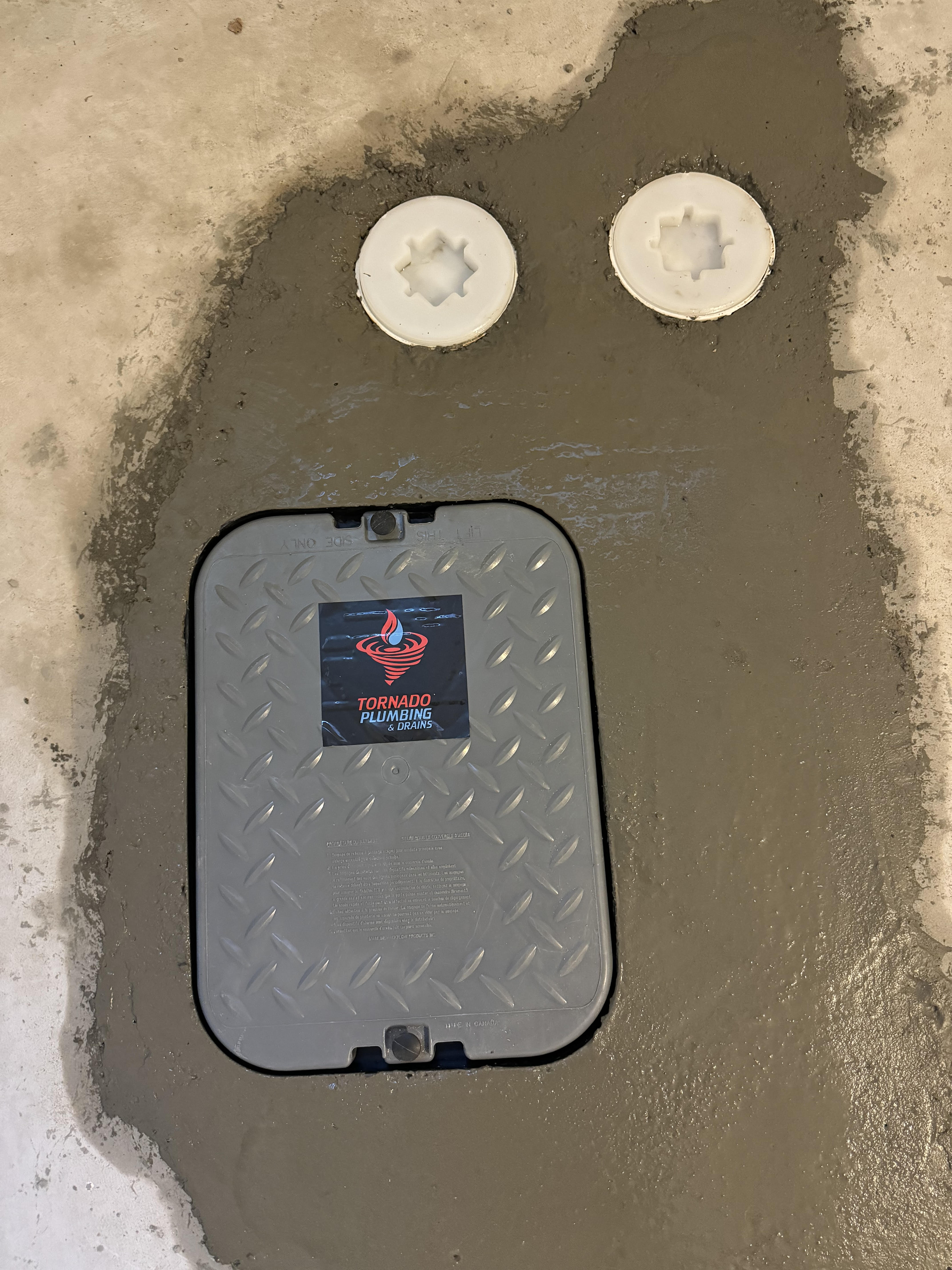 Backwater valve access cover and cleanout caps set in fresh concrete after basement flood-protection work