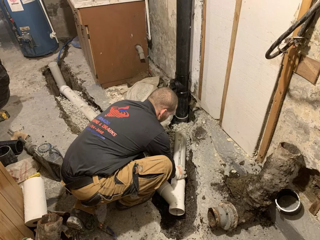 Technician installing basement drain piping in an open concrete floor