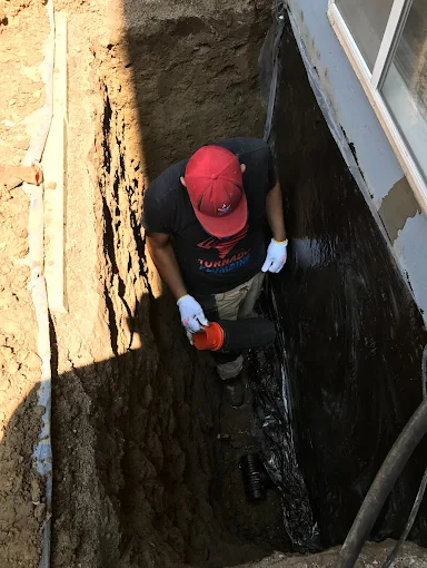 Exterior foundation trench opened beside a home before waterproofing membrane and drainage work